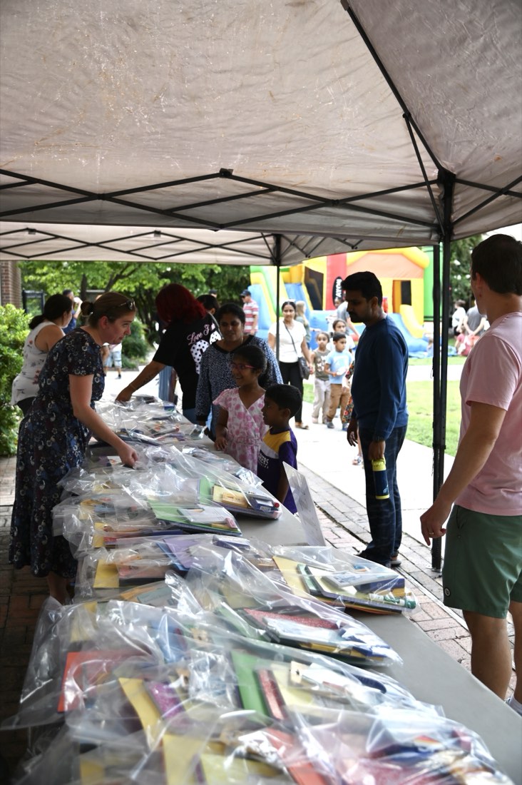 Kids and parents at a long table of bagged school supplies under a white tent.